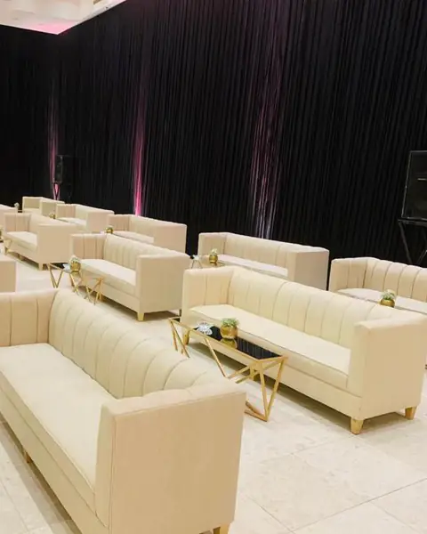 أرائك كريمية وطاولات ذهبية في قاعة بستائر داكنة