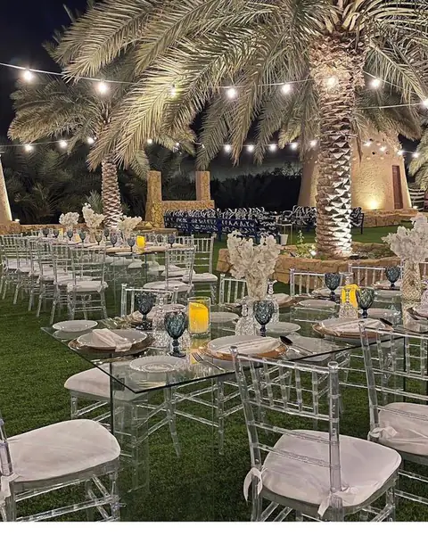 طاولات وكراسي شفافة على العشب ليلًا تحت أضواء معلّقة