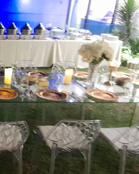 طاولات بوفيه بمفارش بيضاء وزهور وكراسي شفافة على العشب