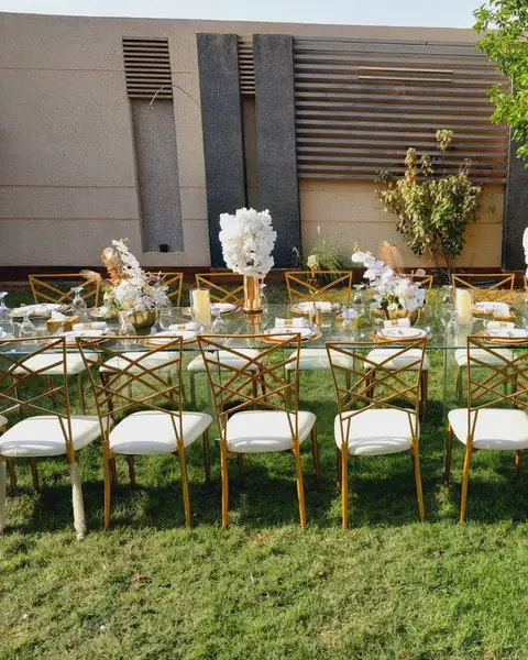 طاولة عشاء طويلة على العشب بكراسي بيضاء وذهبية