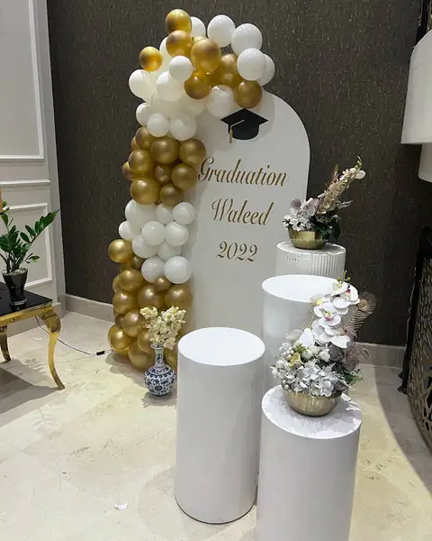 لوحة تخرّج ببالونات ذهبية وبيضاء ومنصّات بيضاء