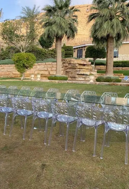 كراسي شفافة مصفوفة على جانبي طاولة زجاجية فوق العشب
