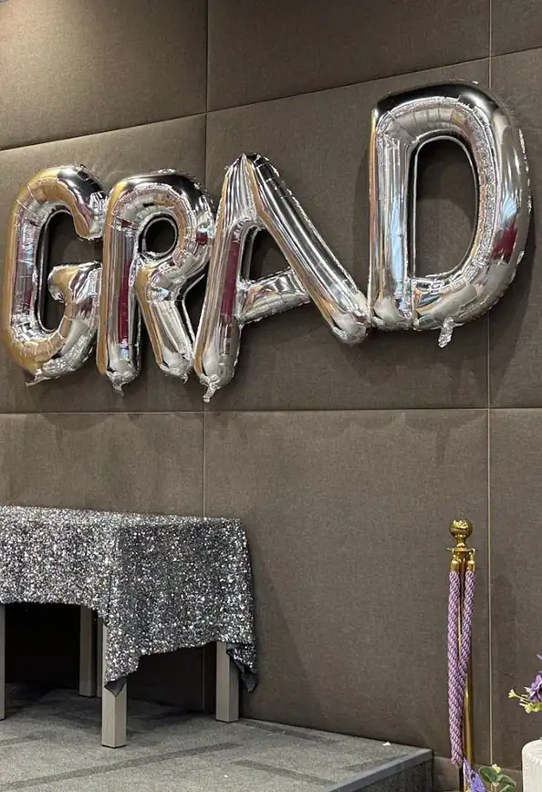بالونات فضية على شكل كلمة GRAD وطاولة بقماش لامع وشجرة زينة