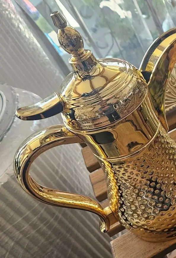 دلة ذهبية وطبق تمر بغطاء شفاف على طاولة خشبية