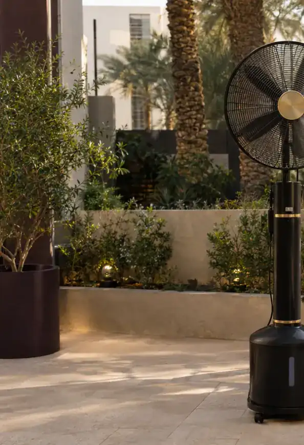 مروحة رذاذ قائمة تنشر رذاذاً ناعماً بجانب جلسة خارجية