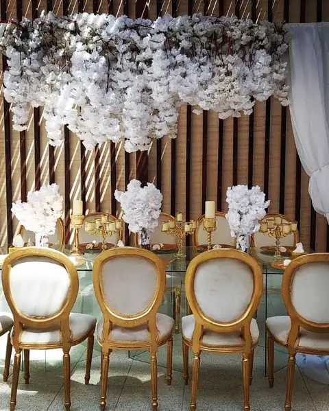 A wedding table with gold chairs under a ceiling of white blossom