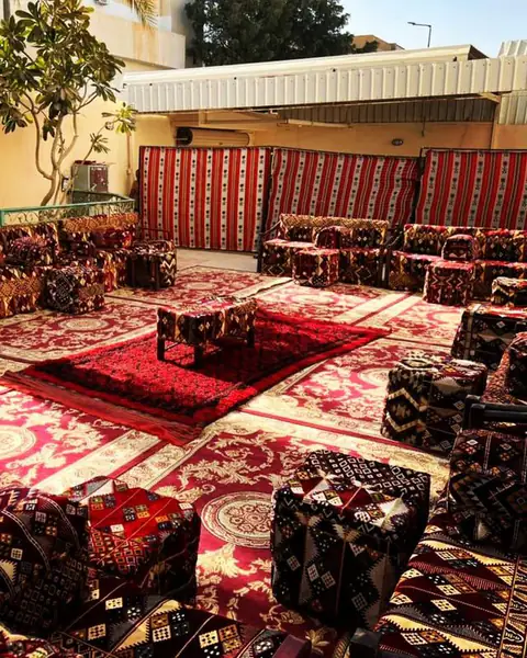 مجلس بجلسات أرضية بوسائد حمراء مطرزة وسجاد في فناء مفتوح