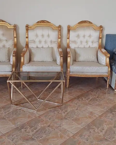ثلاثة كراسي بذراعين بإطار ذهبي حول طاولة زجاجية