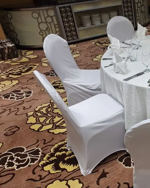 طاولة مستديرة بمفرش أبيض وكراسي مكسوة بأغطية بيضاء فوق سجاد مزخرف