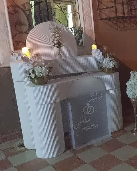 طاولة استقبال بيضاء مع شموع وزهور وقاعدة عرض مدرجة