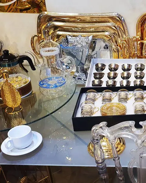 طاولة زجاجية عليها صواني ذهبية وفناجين وحلويات