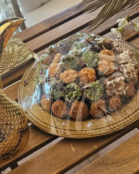 دلة ذهبية وطبق تمر بغطاء شفاف على طاولة خشبية