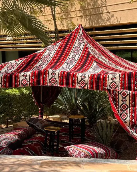 خيمة سرادق حمراء مزخرفة فوق جلسة أرضية بين النخيل