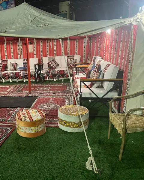 مظلة خضراء فوق جلسة بسجاد أحمر على عشب صناعي