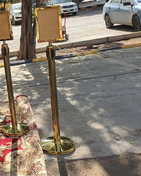 أعمدة تنظيم ذهبية بلوحات إرشادية فوق سجاد أحمر في الهواء الطلق